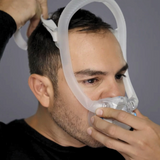 Man adjusting CPAP mask on face for sleep apnea therapy against gray background.