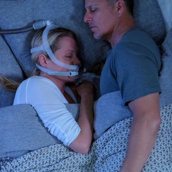 Couple sleeping in bed, woman wearing a CPAP mask for sleep apnea therapy.