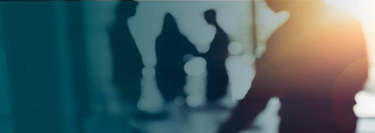 Blurred silhouettes of people in an office setting with sunlight shining through windows.