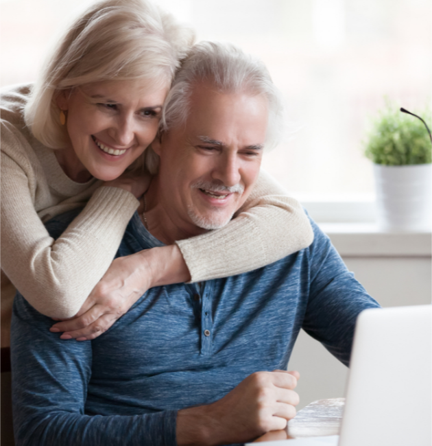 Senior couple smiling while looking at a laptop together in a bright room with a plant in the background.