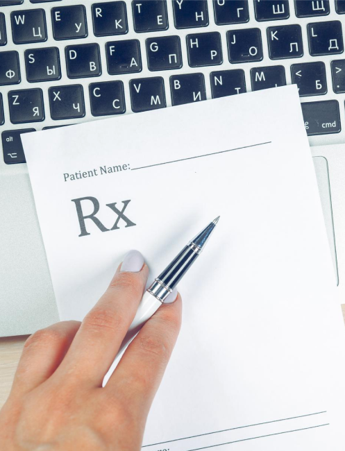 Hand holding a pen over a prescription form on top of a laptop keyboard with Cyrillic characters.